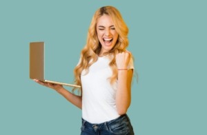 Frau mit langen blonden Haaren hält Laptop in der rechten Hand und ballt die linke Hand zur Siegerfaust